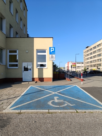 Obraz przedsatwie miejsce parkingowe dla osoób niepełnosprawnych. Miejsce jest oznakowane - niebieską farbą i znakiem drogowy.